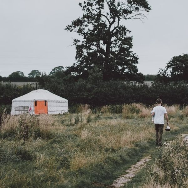 white yurt tent with orange door along grassy path with man walking