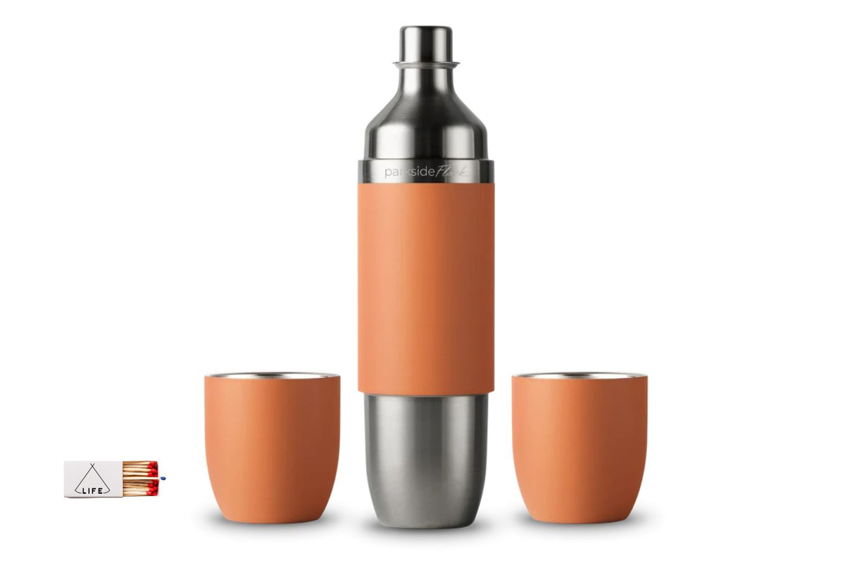 A stainless steel parkside wine flask with an orange color, shown with two matching orange cups and a small matchbox accessory on a white background.