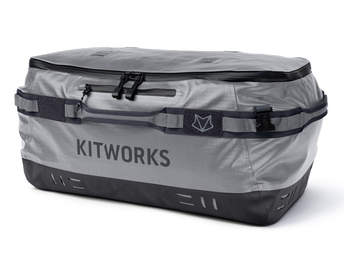 A Kitworks waterproof luggage bag in gray and black, featuring a top zipper, a front hook-and-loop strap with a logo patch, and a dark bottom panel, shown on a white background.