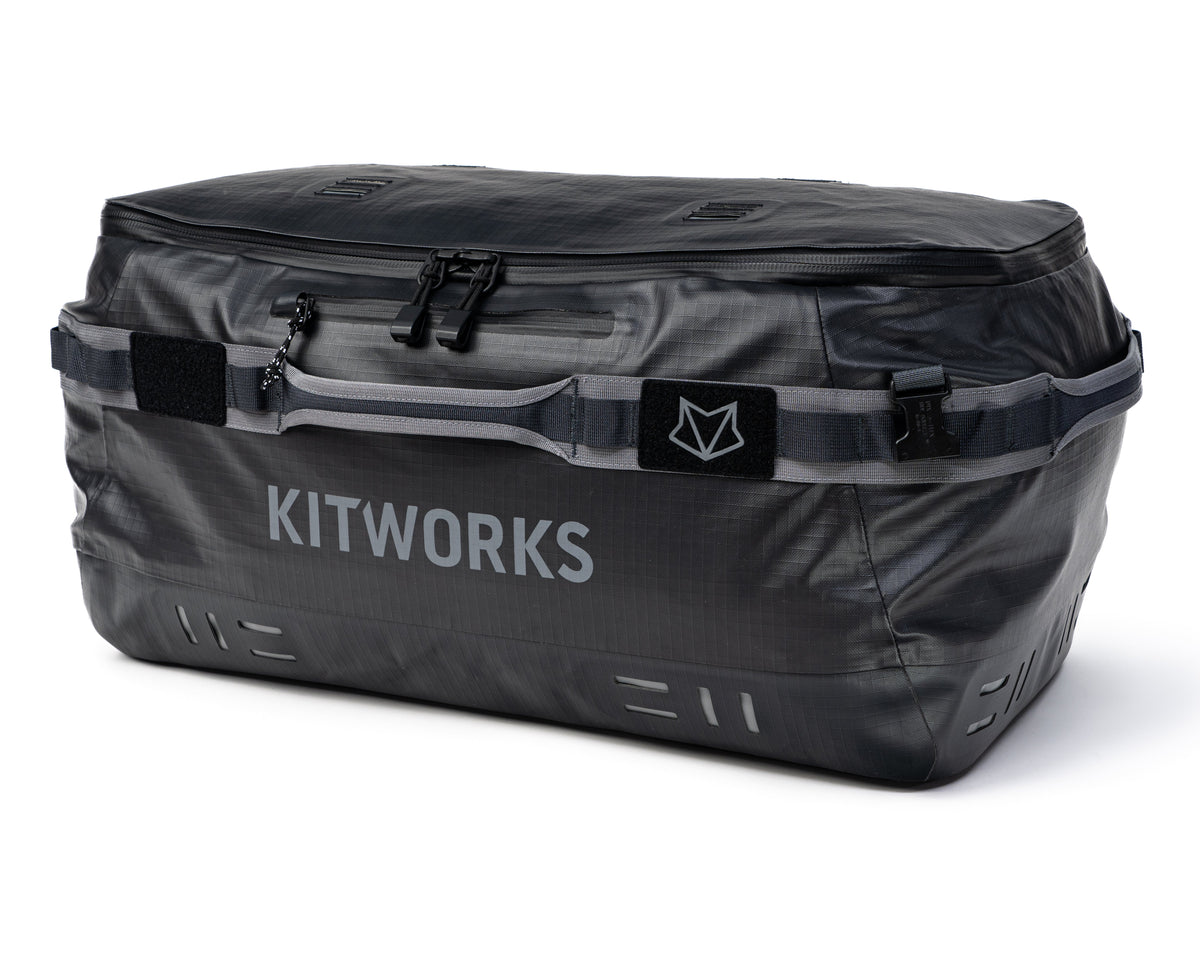 A dark gray waterproof duffel bag with 'KITWORKS' printed in white on the front, featuring a gray carrying strap with a black logo patch, set against a plain white background.