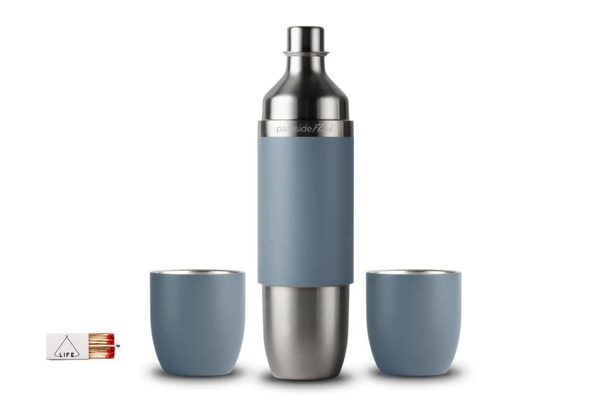 A stainless steel and slate blue insulated wine bottle with two matching blue tumblers, shown on a clean white background. A small matchbox-style product tag is visible at the bottom left.