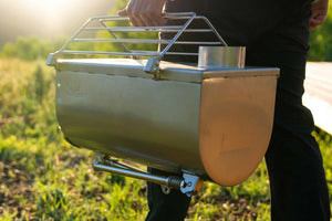 Portable tent stove held by a person outdoors with grass in the background
