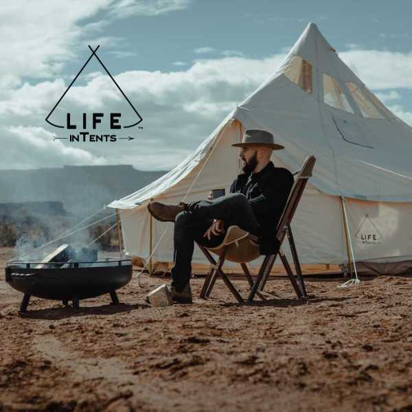 canvas camping tent with man sitting in front of campfire