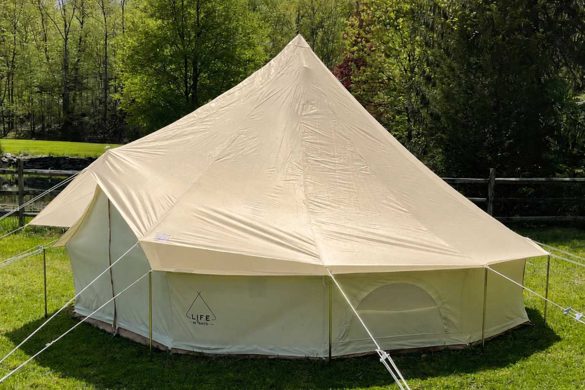 Beige bell tent fly cover over 'LIFE' bell tent on a grassy field with trees in the background