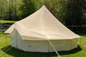 Beige bell tent fly cover over 'LIFE' bell tent on a grassy field with trees in the background