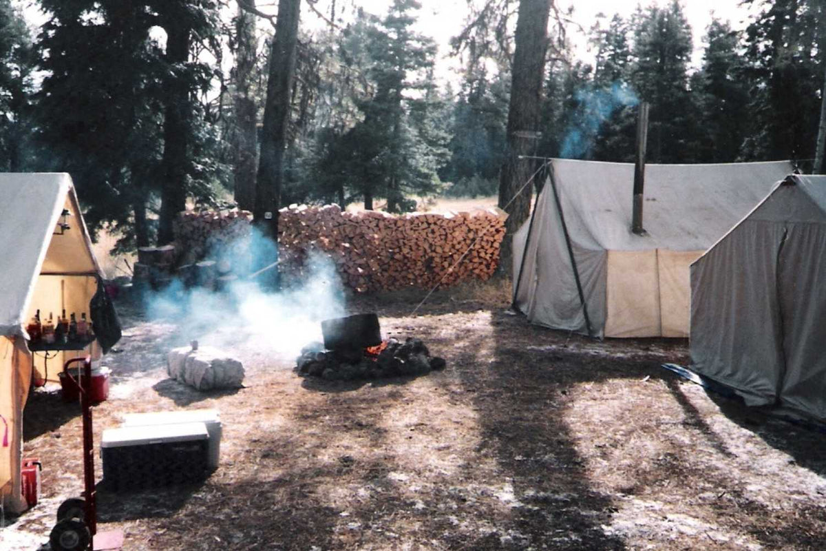 hunting camp with multiple canvas tents and campfire during the day