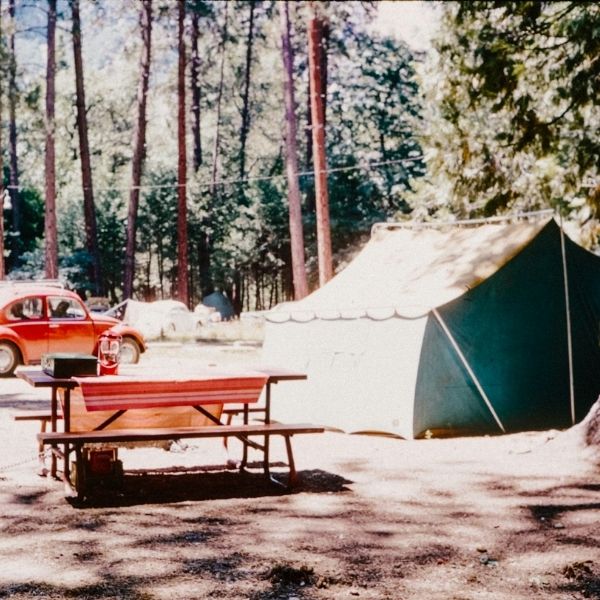 old photo of campsite with green canvas tent, red Beetle Volkswagen, and picnic table