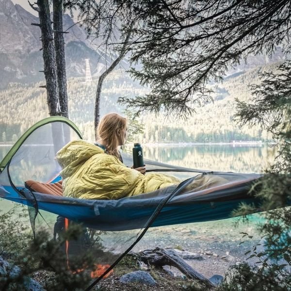 woman hammock camping in sleeping bag with coffee thermos