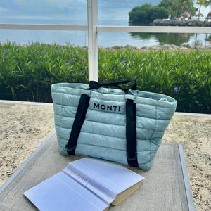 Light blue quilted bag with black straps on a table outdoors by a body of water.