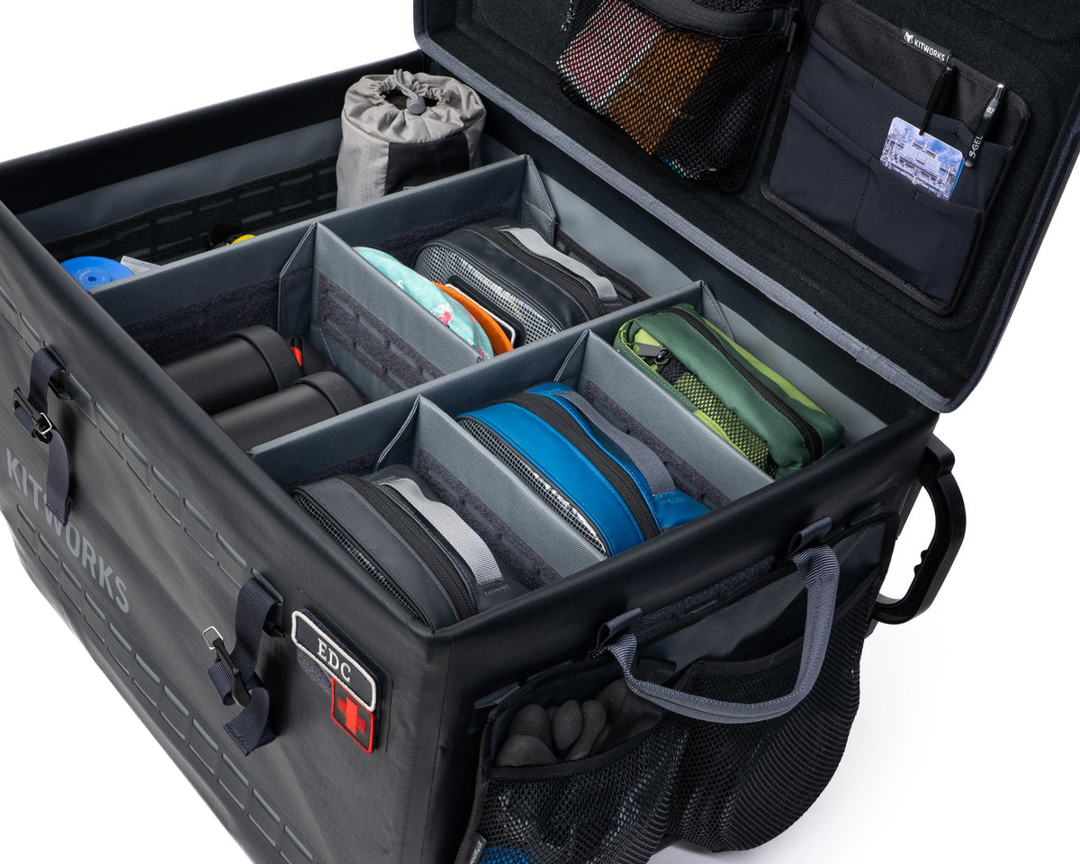 Open black camping case with compartments containing various items on a white background