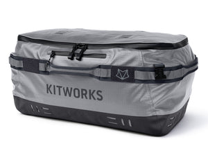 A Kitworks waterproof luggage bag in gray and black, featuring a top zipper, a front hook-and-loop strap with a logo patch, and a dark bottom panel, shown on a white background.