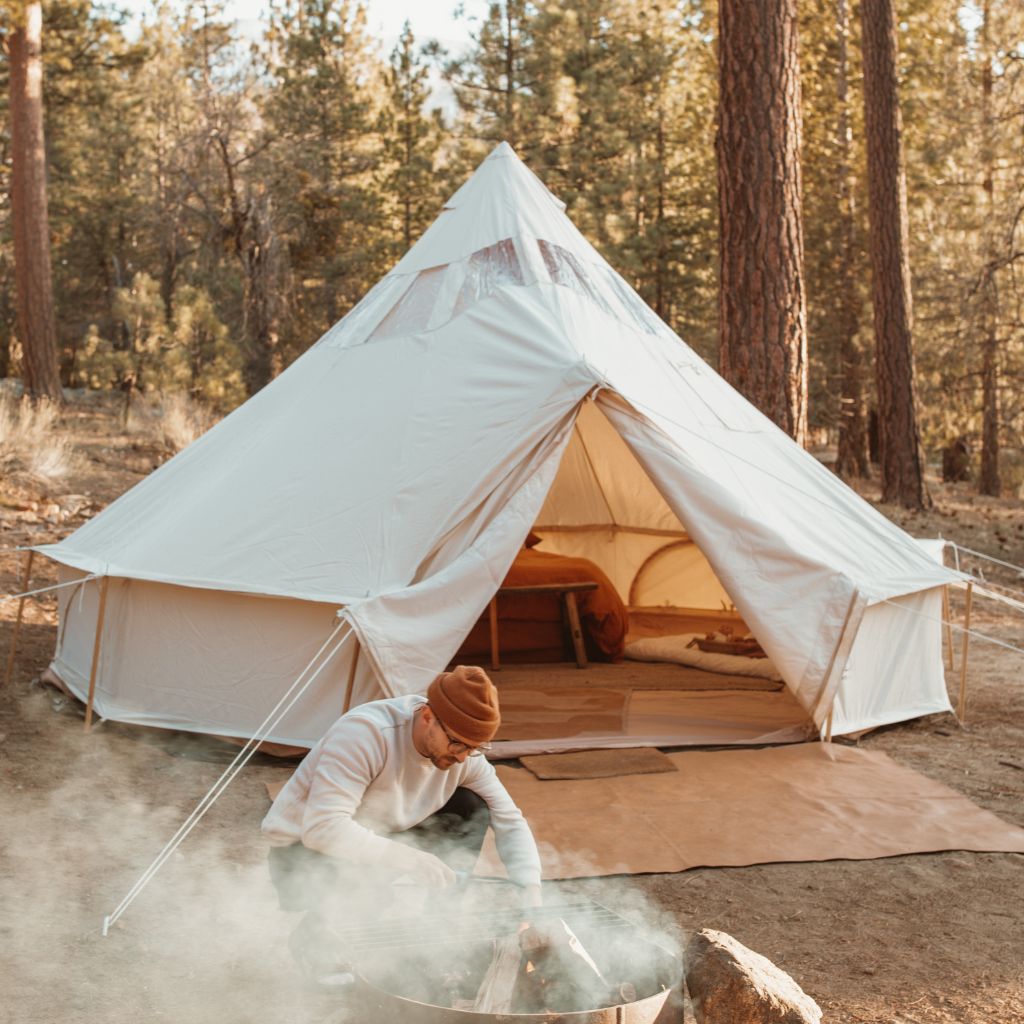canvas tent with man starting a camp fire