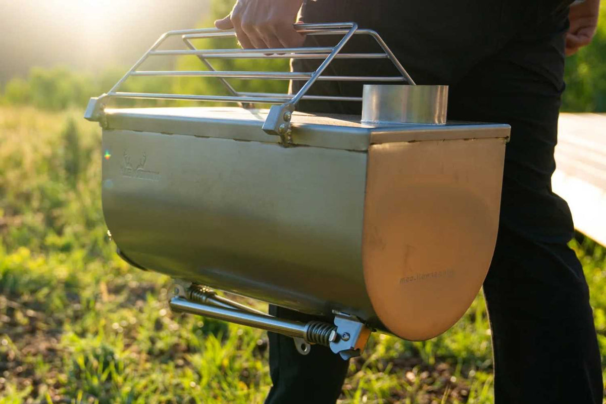 Portable tent stove held by a person outdoors with grass in the background