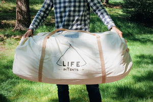 man holding a large canvas bag with a tent inside it