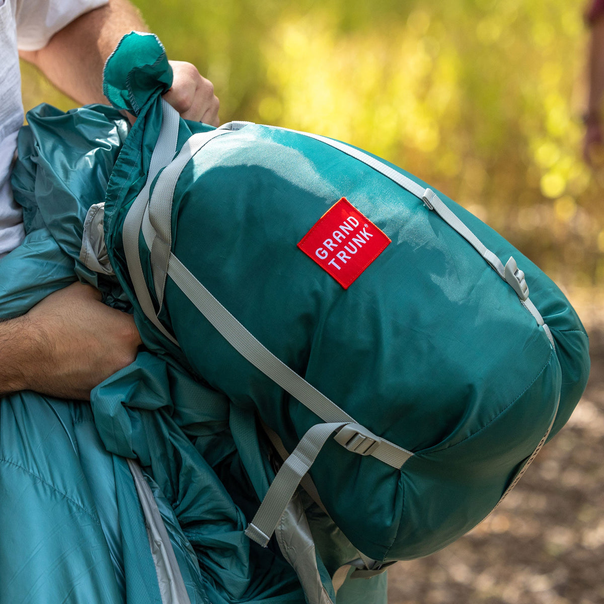 Teal backpack with a red 'Grand Trunk' label held by a person outdoors.