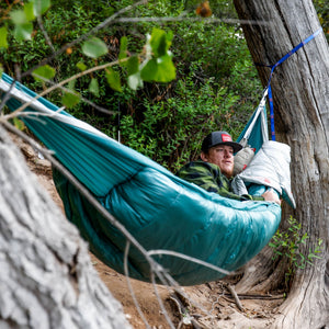 Person in a teal hammock surrounded by trees and nature