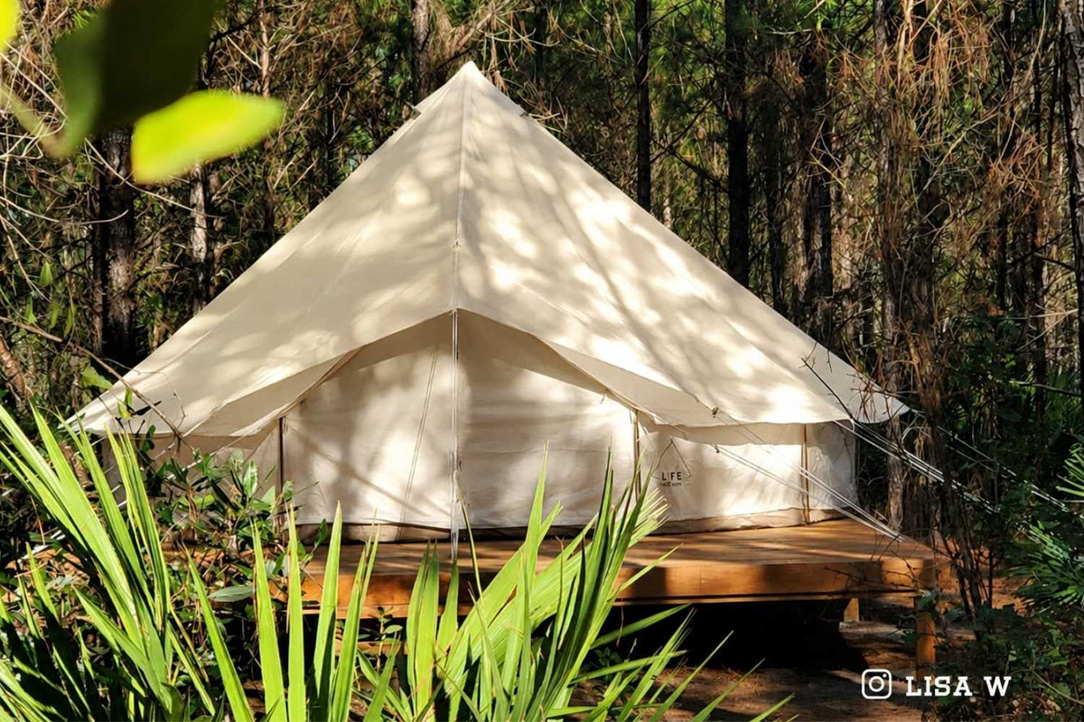 White bell tent on a wooden platform surrounded by greenery in a forest setting