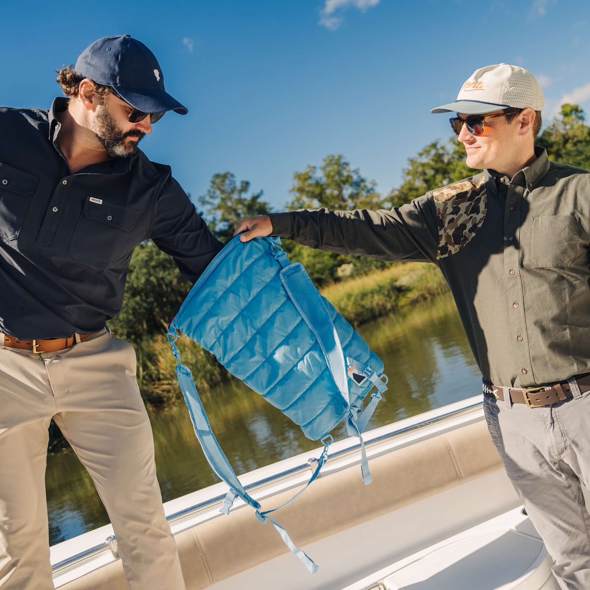 Two men on a boat holding a blue cooler with a scenic background