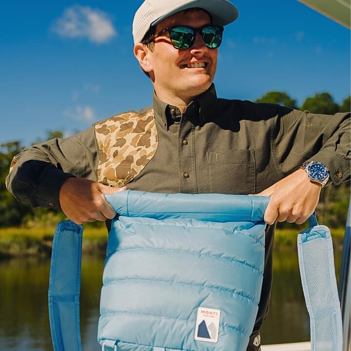 Man holding a blue cooler with a scenic background