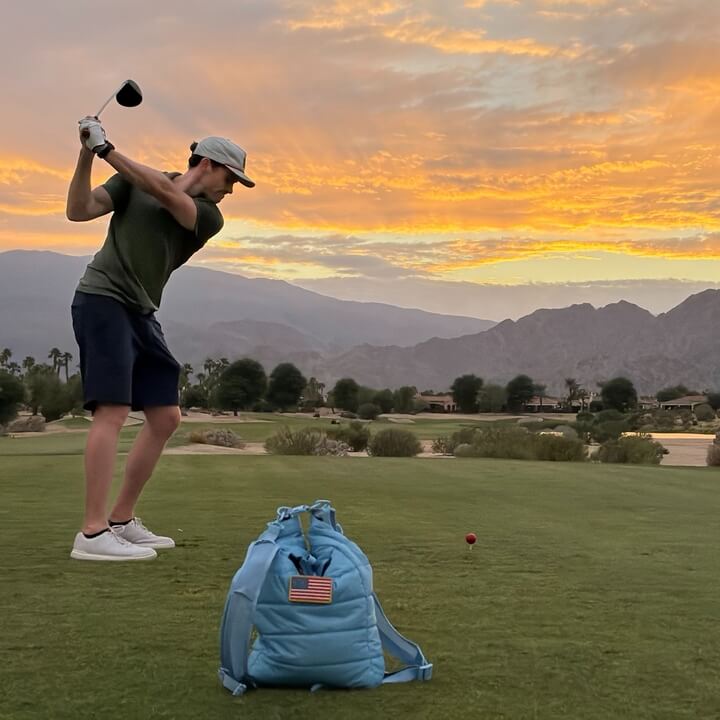 Person playing golf on a scenic course with mountains and sunset in the background