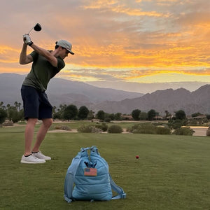 Person playing golf on a scenic course with mountains and sunset in the background