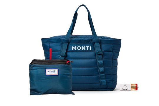 A dark blue Monti cooler tote bag with white logo text, shown next to its matching blue zippered pouch and a small white and red LIFE matchbox on a white background.